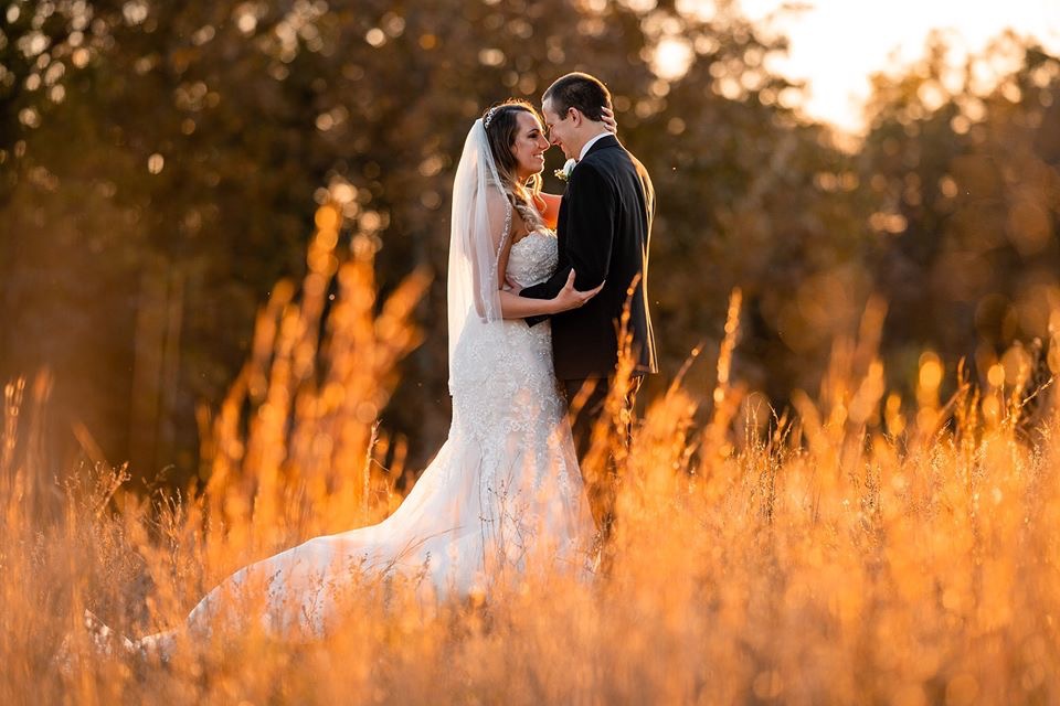 BRIDE AND GROOM IN FIELD AT SUNSET